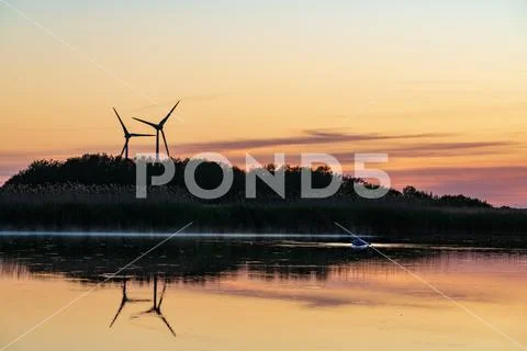 Evening sunlight on coast, pink and golden clouds and wind turbine. Sky refle Stock Photos