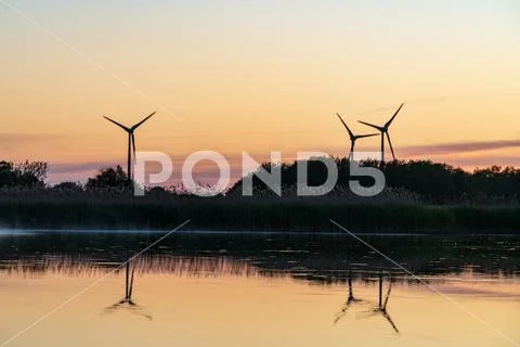 Evening sunlight on coast, pink and golden clouds and wind turbine. Sky refle Stock Photos