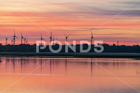 Evening sunlight on coast, pink and golden clouds and wind turbine. Sky refle Stock Photos
