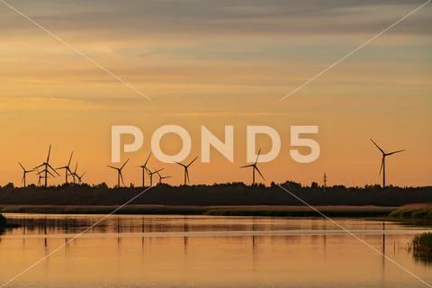 Evening sunlight on coast, pink and golden clouds and wind turbine. Sky refle Stock-Fotos