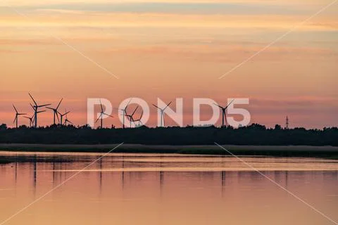 Evening sunlight on coast, pink and golden clouds and wind turbine. Sky refle Stock Photos