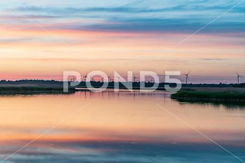 Evening sunlight on coast, pink and golden clouds and wind turbine. Sky refle Stock Photos