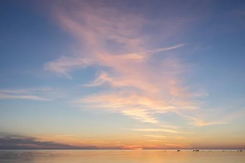 Evening sunlight on coast, pink clouds, blue sky reflection on water. Beach i Stock Photos