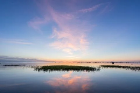 Evening sunlight on coast, pink clouds, blue sky reflection on water. Beach i Stock Photos