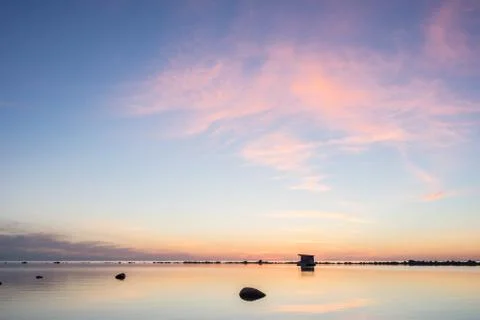 Evening sunlight on coast, pink clouds, blue sky reflection on water. Beach i Stock Photos