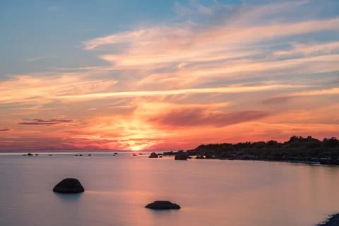 Evening sunlight on coast, pink clouds, blue sky reflection on water. Beach i Stock Photos