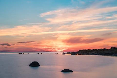 Evening sunlight on coast, pink clouds, blue sky reflection on water. Beach i Stock Photos