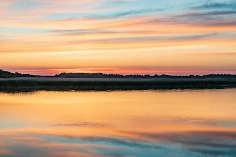 Evening sunlight on coast, pink clouds, blue sky reflection on water. Beach i 스톡 사진