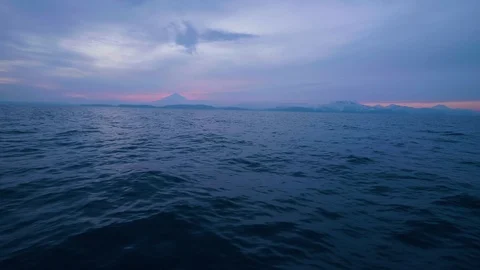Evening sunset in sky with clouds over mountain and blue sea waves on surface Stock Footage 98749691