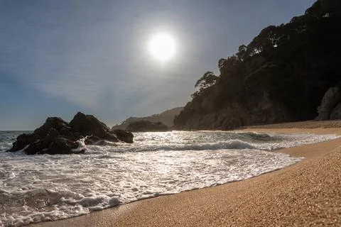 Evening time with sun setting on the beach with dark rocks in sea and hill at Stock Photos