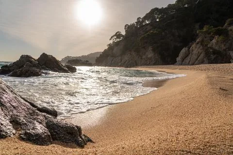 Evening time with sun setting on the beach with dark rocks in sea and hill at Stock Photos