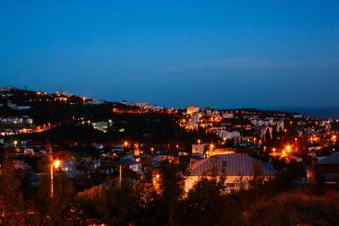 Evening view of hillside town with glowing streetlights. Buildings dot the Stock Photos
