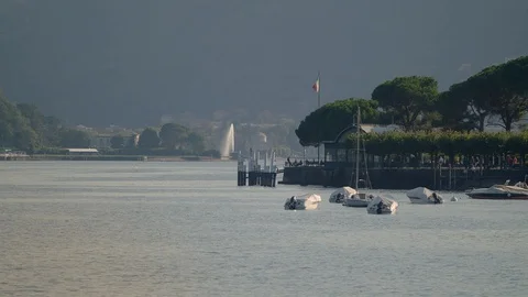 Evening view of pier on Lake Como, with covered boats, fountain, Italian flag Stock Footage 128428998