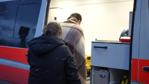 In the evening, when snowflakes are falling, a paramedic helps a man wrapped in Stock Footage 254198044