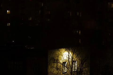 Evening windows illuminated by a lantern behind a tree Stock Photos