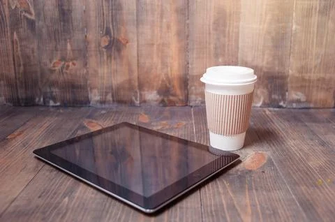 Every day essentials. Paper cup of coffee and tablet computer on the wooden b Stock Photos