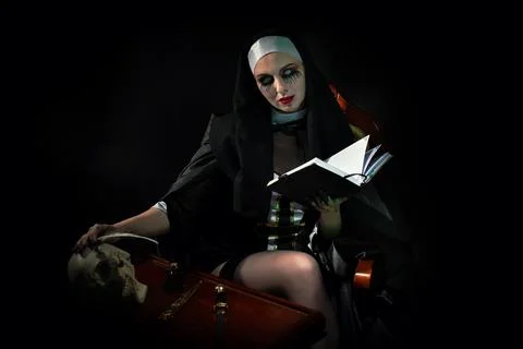 An evil cursed nun with a notebook and a cross in her hands looks at the camera Stock Photos
