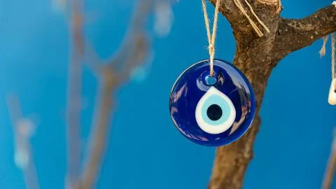 Evil eye bead hanging on the tree, space for text with blue background Stock Photos