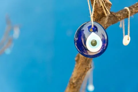 Evil eye bead hanging on the tree, space for text with blue background Stock Photos