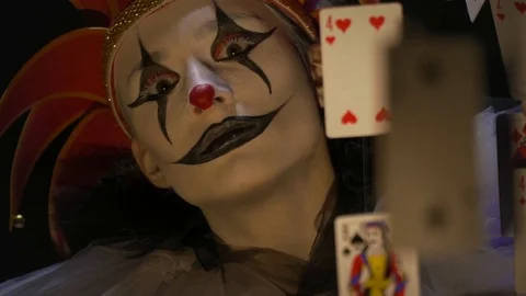 Evil jester with white and black makeup is lurking behind the cards, close up Stock Footage 104648601