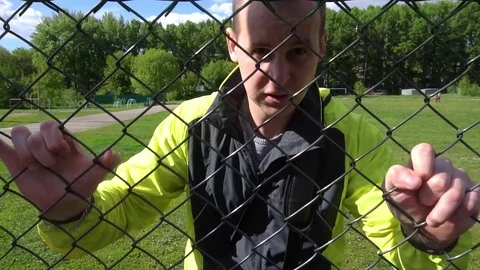 Evil Man in his 20s, leaning against the fence, trying to get out Stock-Footage 75915261