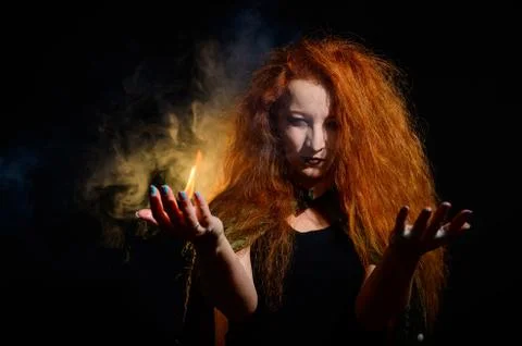 An evil red-haired witch holds fire in her hands. Stock Photos