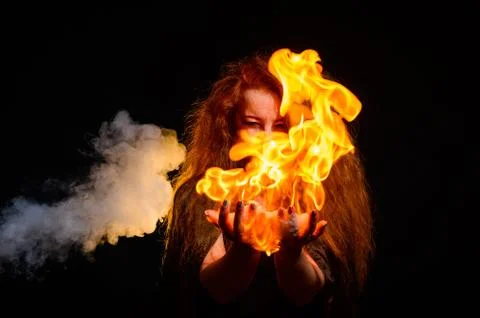 An evil red-haired witch holds fire in her hands. Stock Photos