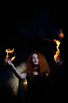 An evil red-haired witch holds fire in her hands. Stock Photos