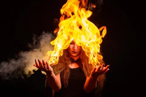 An evil red-haired witch holds fire in her hands. Stock Photos