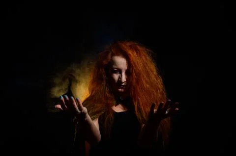 An evil red-haired witch holds fire in her hands. Stock Photos