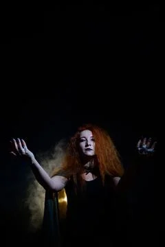 An evil red-haired witch holds fire in her hands. Stock Photos