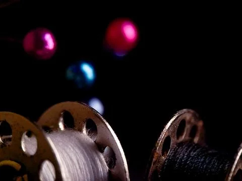 Evocative low-key photograph displaying spools of thread and sewing pins on.. Stock Photos