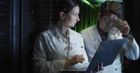 Examining lab coat duo inspecting laptop in server room, with LED racks and w Stock Photos