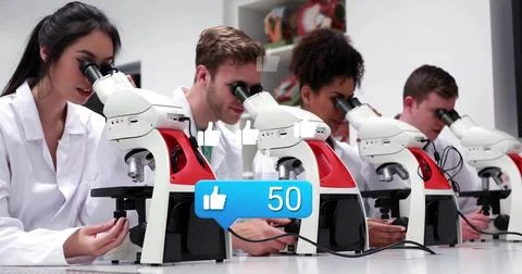 Examining students using white-red compound microscopes in lab in lab coats and Stock Photos
