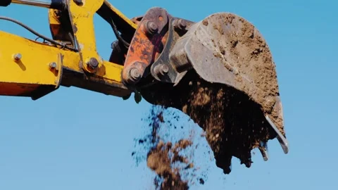 Excavator bucket dumping earth at construction site against clear blue sky. Vídeos de archivo 334559794