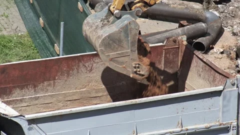 Excavator bucket pours dirt into dump truck bed at construction site during day. Stock Footage 344864027