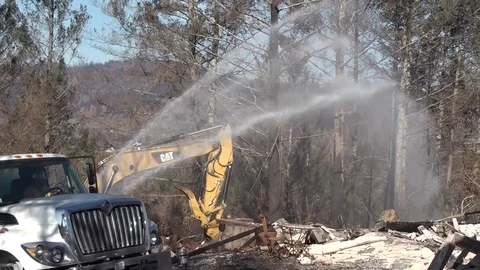 Excavator clearing rubble after fire with water sprayed onto rubble. Stock Footage 84625422