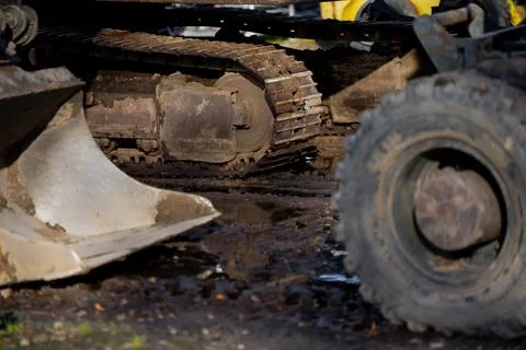Excavator crawler track system and loader wheel in muddy construction site Stock Photos