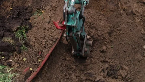 Excavator digging alongside red pipe in soil on grassy patch at construction Vídeos de archivo 291123105