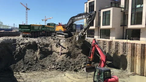 Excavator is digging a big hole in the ground in a residential area Stock Footage 133447194