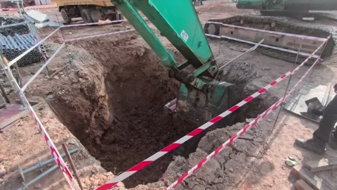 Excavator Digging Deep Hole for Electrical Manhole Installation with Safety Tape Stock Footage 340985864