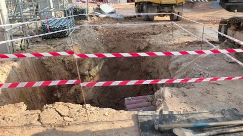 Excavator Digging Deep Hole for Electrical Manhole Installation with Safety Tape Stock Footage 340985952