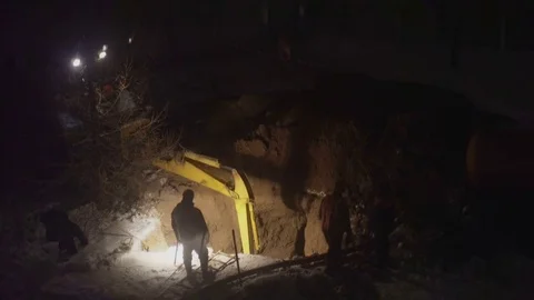 An excavator digging a pit and workers stand around at night Stock Footage 72450073