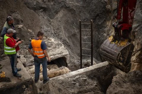 Excavator digging a pit. Three workers looking on ladle. Stock Photos