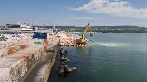 An excavator diligently constructs a dock or breakwater in the sea, its mighty Stock Footage 242591597