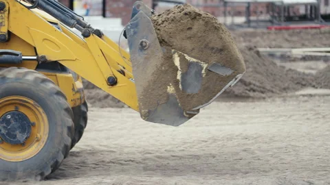 An excavator equipped with a bucket is actively loading sand at a bustling Stock Footage 312635624