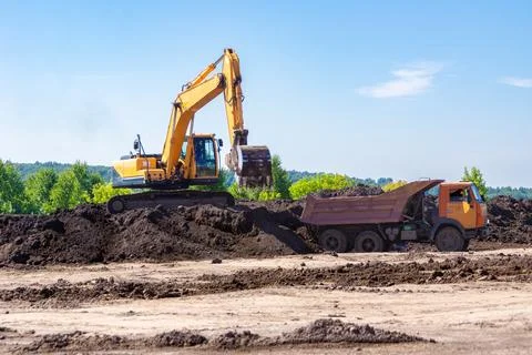 Excavator loading black earth onto dump truck for topsoil conservation before Stock Photos