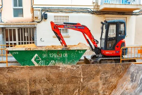 Excavator Loading Sand Into a Green Dumpster on a Construction Site in an Urban Stock Photos