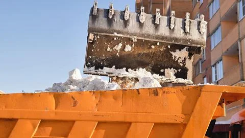 Excavator loading snow into a dump truck, city crews clearing winter blizzard Stock Photos