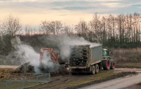 Excavator loads manure, hovering in the cold air, into a trailer Stock Photos